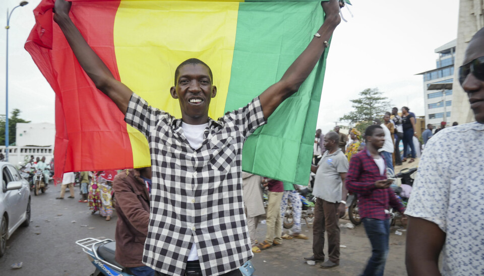 En mann holder opp flagget mens han feirer sammen med andre i gatene i Bamako i Mali. Bildet er datert tirsdag 18. august.
