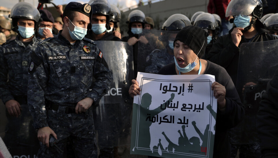 DEMONSTRASJONER: Spesialstyrker omringer en demonstrant som roper slagord mot regjeringen og holder en plakat hvor det står på arabisk: «Forsvinn, slik at Libanon igjen blir en nasjon med verdighet». Demonstrantene mener Libanons politiske lederskap har skyld i den økonomiske og finansielle krisen landet står oppe i.