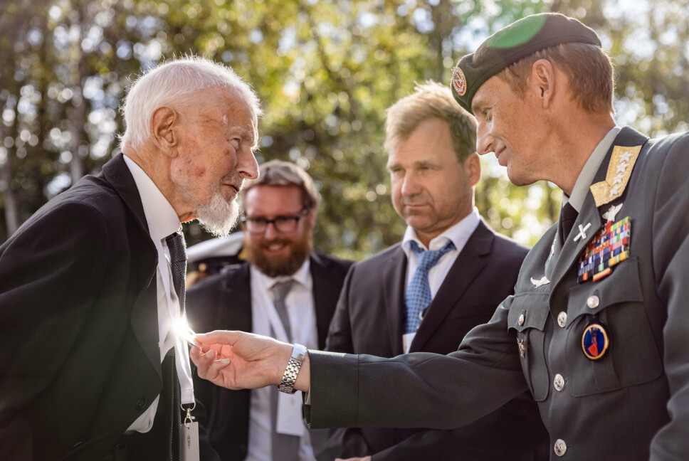 SMYKKE: Forsvarssjef Eirik Kristoffersen og billedkunstner Vebjørn Sand tar en titt på kjedet til Eystein Røset (102). I bakgrunnen står barnebarnet til krigsveteranen.