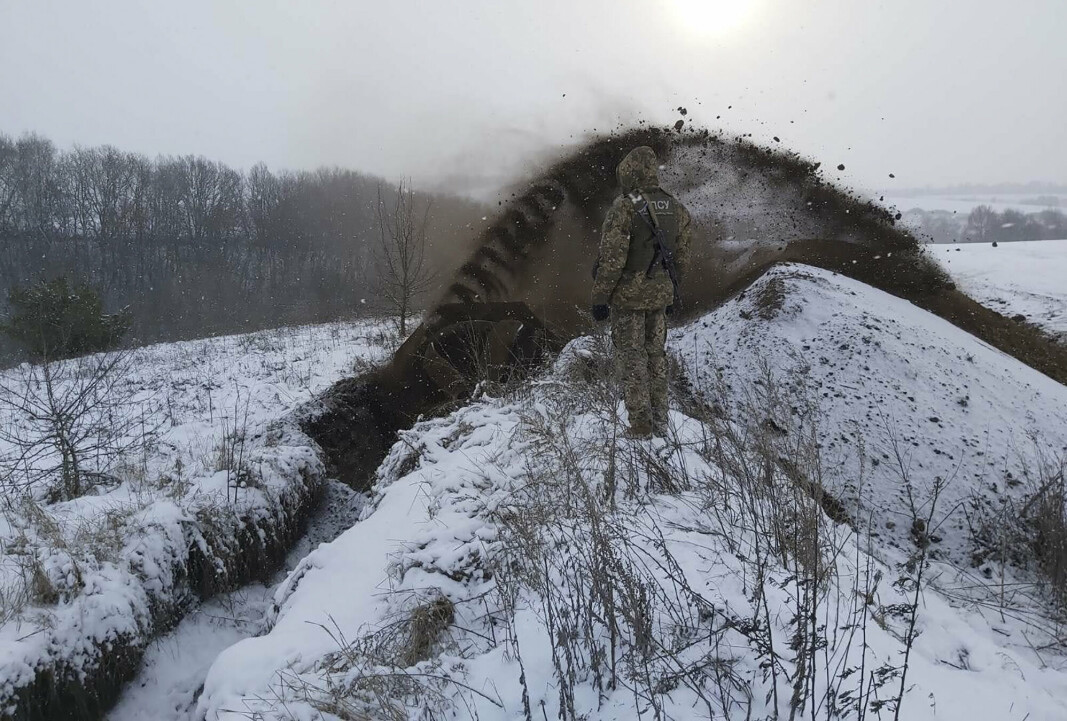 PÅ GRENSEN: Dette arkivbildet er distribuert av den ukrainske grensevakten og viser en vakt som passer på mens et spesialkjøretøy graver en grøft. Bildet er fra Sumy og er datert 21. desember 2021.