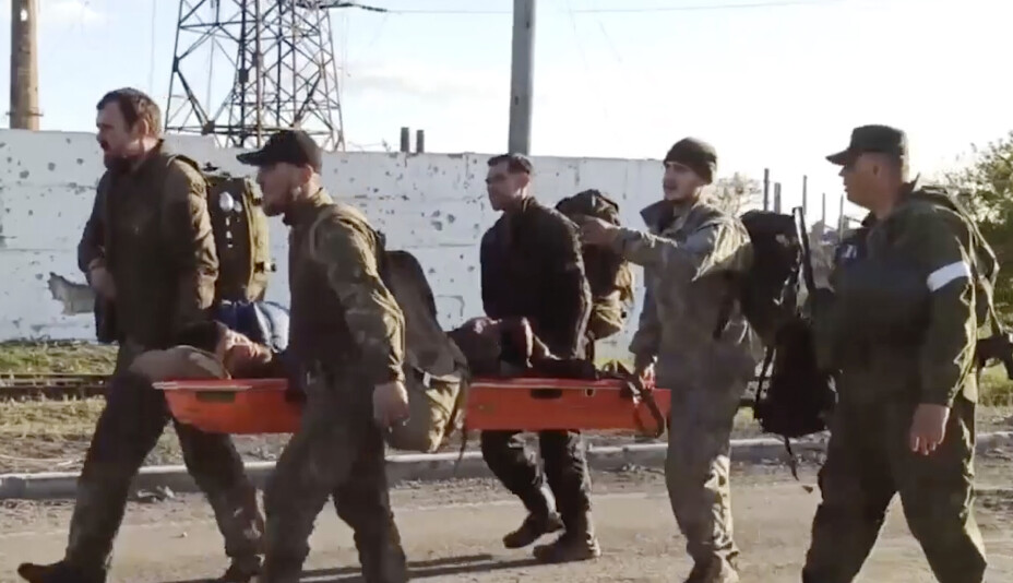 På dette bildet tatt fra en video utgitt av det russiske forsvarsdepartementets pressetjeneste tirsdag 17. mai, bærer ukrainske tjenestemenn en såret kamerat ledsaget av russiske tjenestemenn mens de blir evakuert fra det beleirede Azovstal-stålverket i Mariupol.