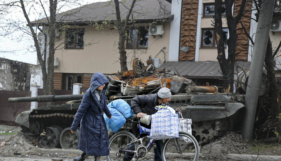 SIVILE: Lokale sivile går forbi en stridsvogn som ble ødelagt under harde kamper i et område kontrollert av russisk-støttede separatiststyrker i Mariupol, Ukraina, 19. april 2022.