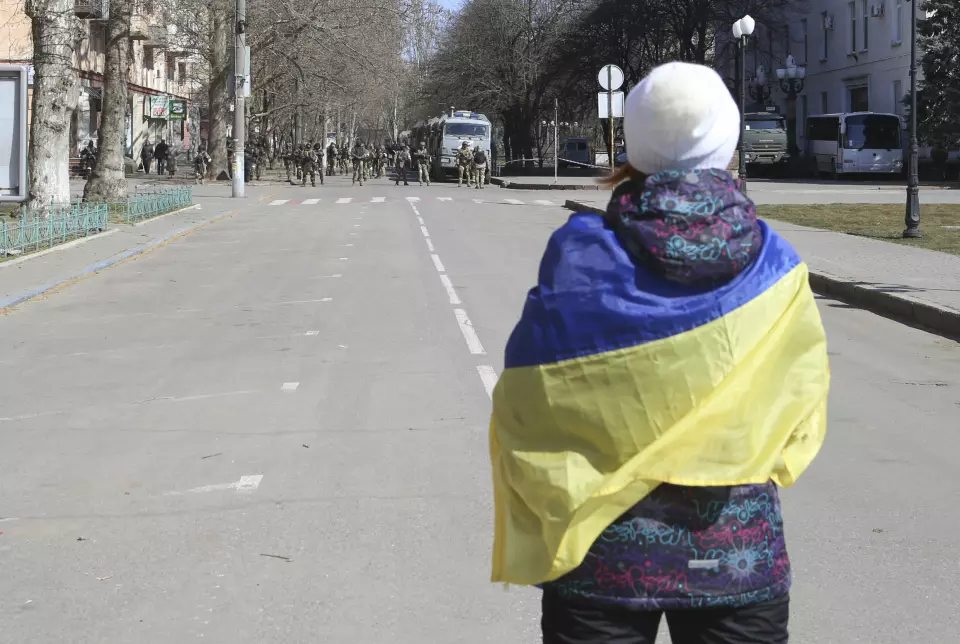 FIL – En kvinne dekket av det ukrainske flagget står foran russiske tropper i en gate under en demonstrasjon mot russisk okkupasjon i Kherson, Ukraina, 19. mars 2022.