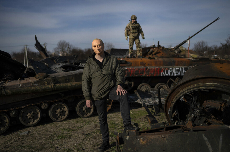 MASKE: En mann poserer for fotografen iført en Putin-maske, utenfor Kyiv i april 2022. I bakgrunnen står en ukrainsk soldat på toppen av en russisk stridsvogn som ble ødelagt under kampene i Bucha.