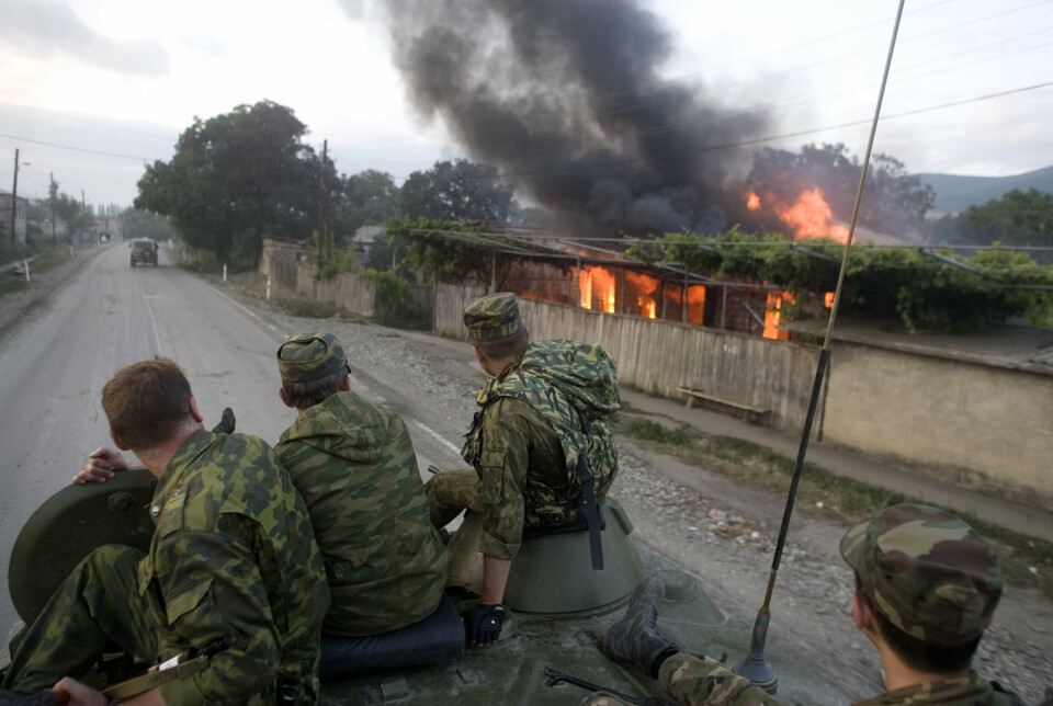 ØDELEGGELSER: Russiske soldater kjører forbi et brennende hus på vei til Tskhinvali i Sør-Ossetia, 11. august 2008.