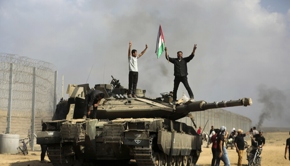 VED GRENSEN: Palestinere vifter med det palestinske flagget på en ødelagt israelsk stridsvogn på Gazastripen, ved grensegjerdet øst for Khan Younis sør i enklaven lørdag.
