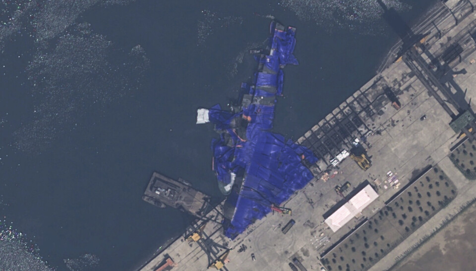 Satellittbilder viser skipet dekket med blå presenninger og veltet på siden, med akterenden i vannet.