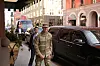 Soldat i kamuflasjeuniform går på fortau ved siden av svart SUV i bygate