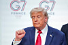Donald Trump står foran G7-bakgrunn og gjør en knyttet hånd-gest etter mediekonferansen.
