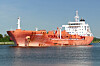 Oransje tankskip på rolig sjø med kystlinje i bakgrunnen.
