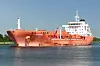 Oransje tankskip på rolig sjø med kystlinje i bakgrunnen.