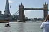 Tower Bridge i London med en båt på Themsen og en person som tar bilde fra høyre side.