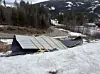 Snødekket konstruksjon med trebjelker i et skogkledd fjellandskap.