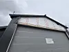 Grå industriport med uferdig fasade sett nedenfra mot en overskyet himmel.
