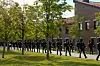 Uniformerte personer går på rekke foran en teglbygning i en park.