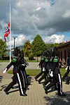 Uniformerte gardister marsjerer på en plass under norsk flagg.