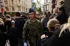 Uniformert soldat står omgitt av sørgende og tilskuere i en bygatesetting.