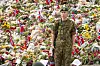 Soldat i kamuflasjeuniform foran et blomsterhav med norske flagg.