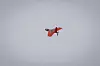 Rød fastvinget drone sett mot en jevn, grå himmel.