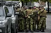 Soldater i kamuflasjeuniform står samlet ved militære kjøretøy i en bygate.